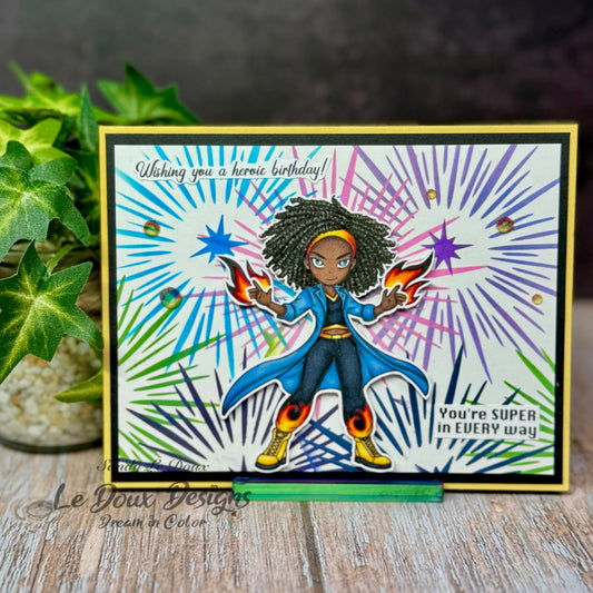 Colorful birthday card with superhero design featuring a character holding flames, on a wooden surface with a plant in the background.