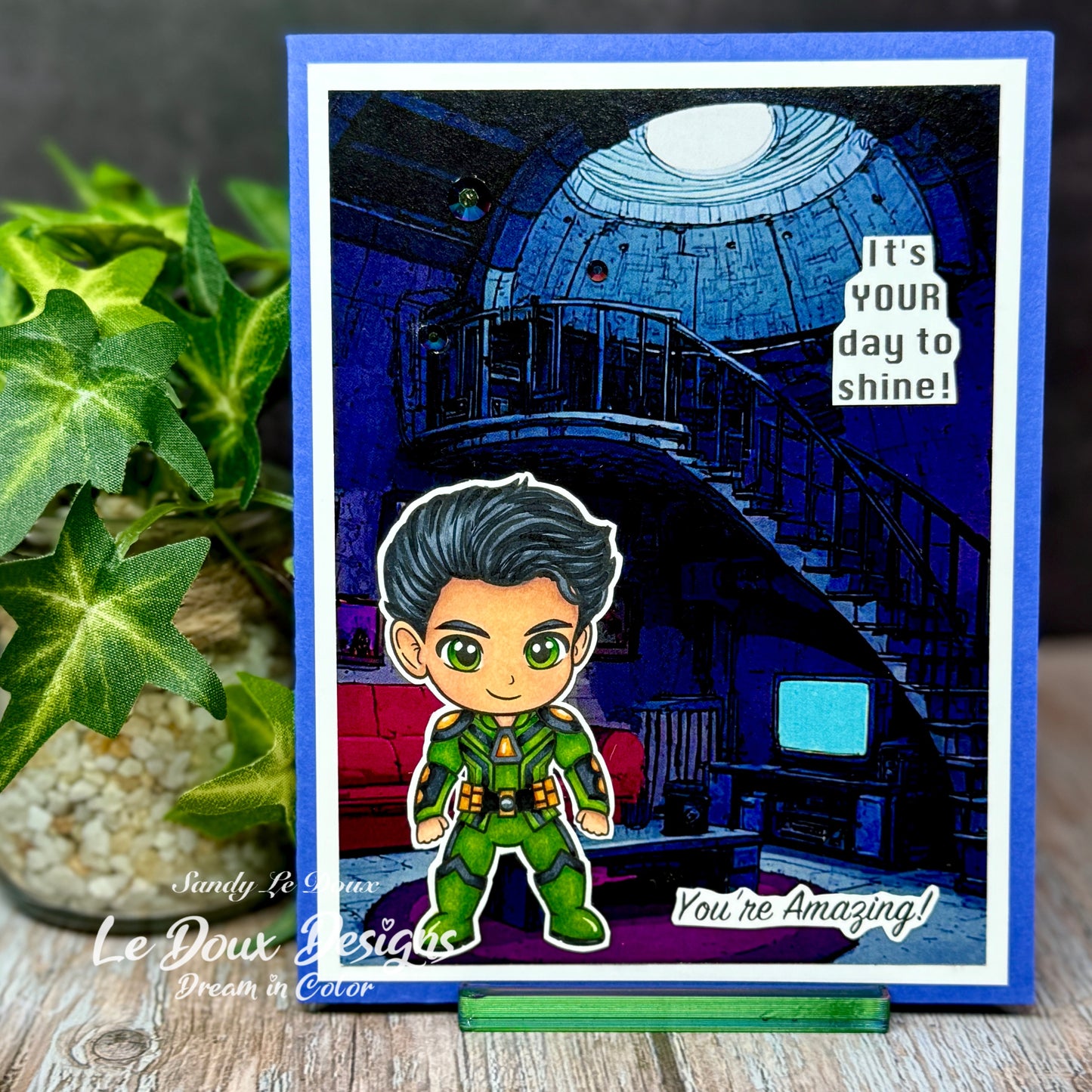 Card with a character in a green outfit and text 'It's YOUR day to shine! You're Amazing!' on a decorative stand.