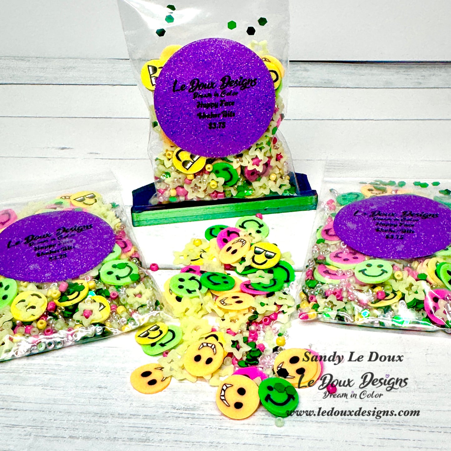 Colorful buttons with smiley face designs in clear bags with purple labels on a white wooden surface.