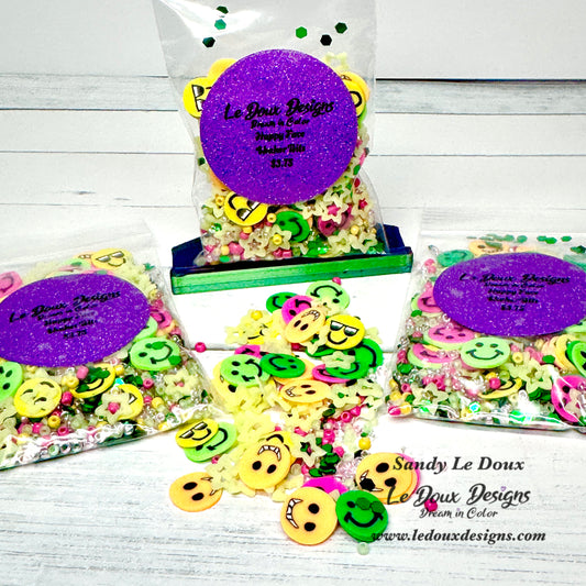 Colorful buttons with smiley face designs in clear bags with purple labels on a white wooden surface.