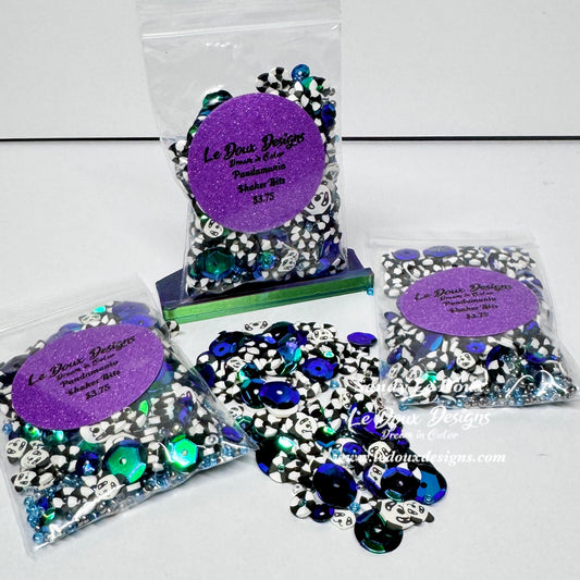 Three clear plastic bags of decorative craft beads with purple glitter round labels, plus loose piles of the beads spread in front on a white surface. The beads are primarily black and white pandas .